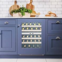 a wine cooler in the middle of a kitchen with blue cabinets and white tile walls