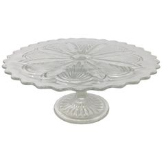 a clear glass cake plate on a white background with an ornate design in the center