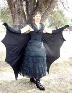 a woman in a black dress is standing under a tree