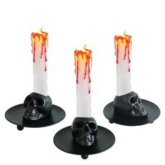 three black candles with red and orange flames on top of each candle holders are decorated with a skull head