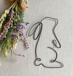 a wire sculpture sitting next to a bunch of flowers on top of a white surface