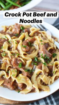 a white plate topped with pasta covered in meat and sauce next to green beans on a wooden table