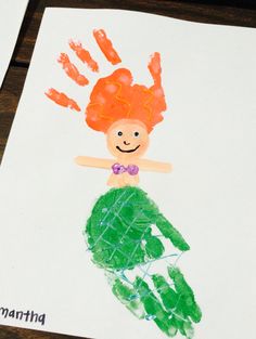 a child's handprint drawing of a mermaid on white paper with orange hair