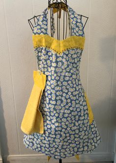 an apron on a mannequin with yellow and blue flowers in the front, next to a white wall