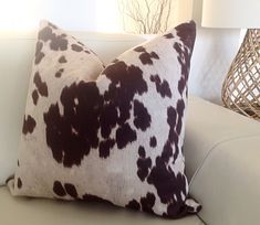 a brown and white cow print pillow sitting on top of a couch next to a lamp