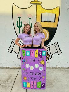 two women standing next to each other in front of a wall with a sign that says, i'd be if you weren