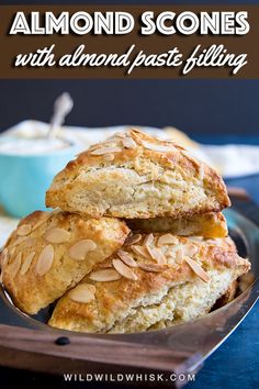 two scones stacked on top of each other with almonds in the background and a bowl of yogurt to the side