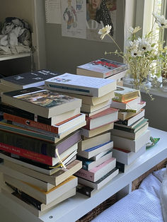 a stack of books sitting on top of a table next to a vase with flowers