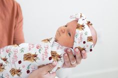 a woman is holding a baby wrapped in a floral print wrap and looking at the camera