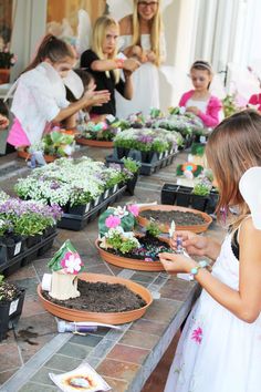 a group of children standing around plants in pots on a table with people looking at them