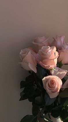 a vase filled with pink roses sitting on top of a table next to a wall