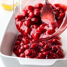 a spoon is pouring red liquid into a white dish filled with cranberry sauce