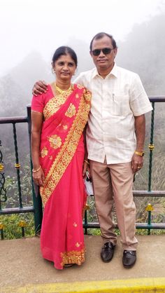 a man and woman standing next to each other on top of a hill with fog in the background