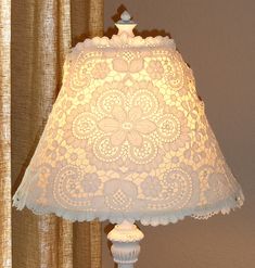 a lamp that is on top of a table next to a window with curtains behind it