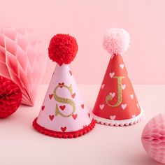 three party hats with red pom - poms on top and pink tissue balls in the background