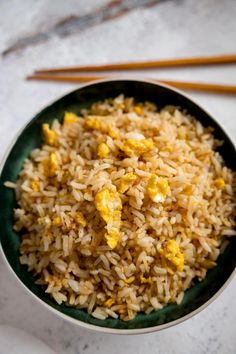 a bowl filled with rice and eggs next to chopsticks on a white surface