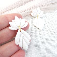 a hand holding two white flower shaped earrings