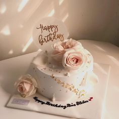 a white cake with pink roses on top and a happy birthday sign in the middle