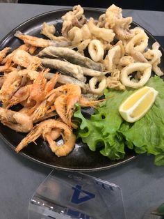 a black plate topped with shrimp, lettuce and lemon wedges on top of a table