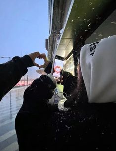 a person holding up a cell phone while standing on a subway platform in the rain