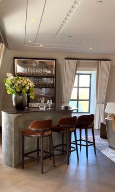 a bar with four stools in front of it and a vase filled with flowers on the counter