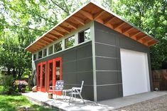 a small gray and red shed with two doors on the side, sitting in front of trees