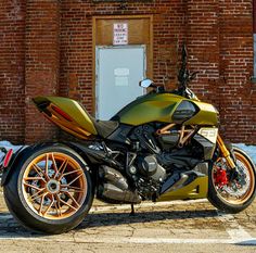 a motorcycle parked in front of a brick building with orange rims on it's tires