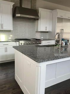 a large kitchen with white cabinets and granite counter tops on the island in front of the sink