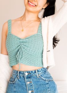 a woman wearing a green crop top and denim skirt with her arms behind her head