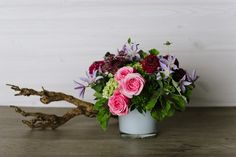 a vase filled with lots of flowers on top of a wooden table next to driftwood