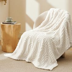 a white blanket sitting on top of a chair next to a wooden table with a cup