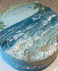 a birthday cake with blue frosting and palm trees on the top is sitting on a table