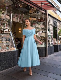 a woman standing in front of a store wearing a blue dress and matching heels with her hand on her hip