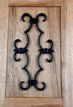 two black wrought iron brackets on a wooden door frame with wood grain flooring behind them