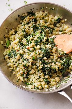 a pan filled with rice and spinach on top of a white counter next to a wooden spoon