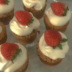 small cupcakes with white frosting and strawberries on top are sitting on a plate