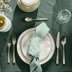 a place setting with silverware and napkins on a green tableclothed table