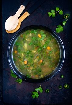 a bowl filled with soup next to a wooden spoon and some parsley on the side