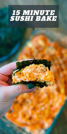 a hand holding up a piece of sushi bake in front of a casserole dish