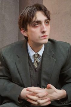 a man in a suit and tie sitting down with his hands folded over his chest