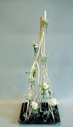 a tall white flower arrangement on a black base with flowers in the center and long stems sticking out of it