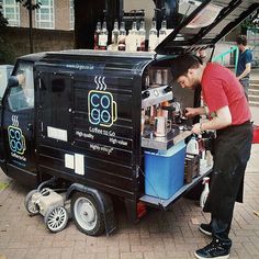 a man standing next to a small cart filled with drinks and coffee machines on the sidewalk