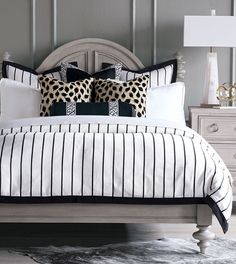 a bed with black and white pillows on top of it next to a night stand