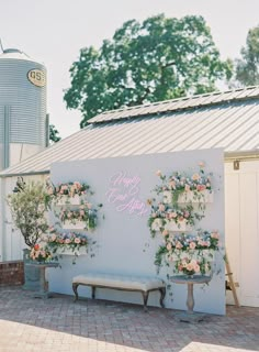 a white wall with flowers on it next to two benches and a silo in the background