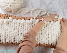 a woman is crocheting on a white and brown blanket with yarn next to it