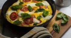 an omelet with tomatoes, cheese and spinach is on a cutting board