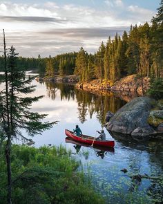 a person in a red canoe on the water near some trees and rocks at sunset