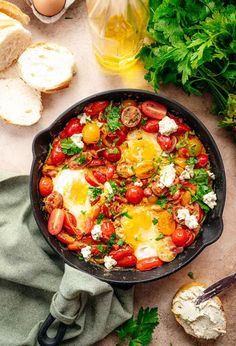 an iron skillet filled with eggs, tomatoes and bread on a table next to parsley