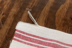 a red and white striped towel sitting on top of a wooden floor next to a pair of scissors