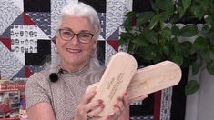 an older woman holding two wooden paddles in front of a quilt